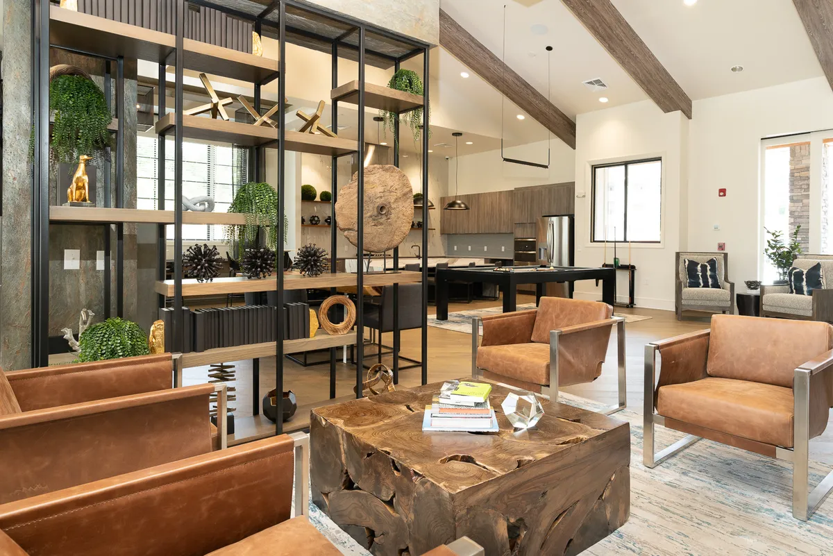 A warm, open-concept space with a visible kitchen area in the background, complemented by a comfortable seating zone with leather chairs and a wooden coffee table. The setup encourages seamless flow between dining, cooking, and socializing.