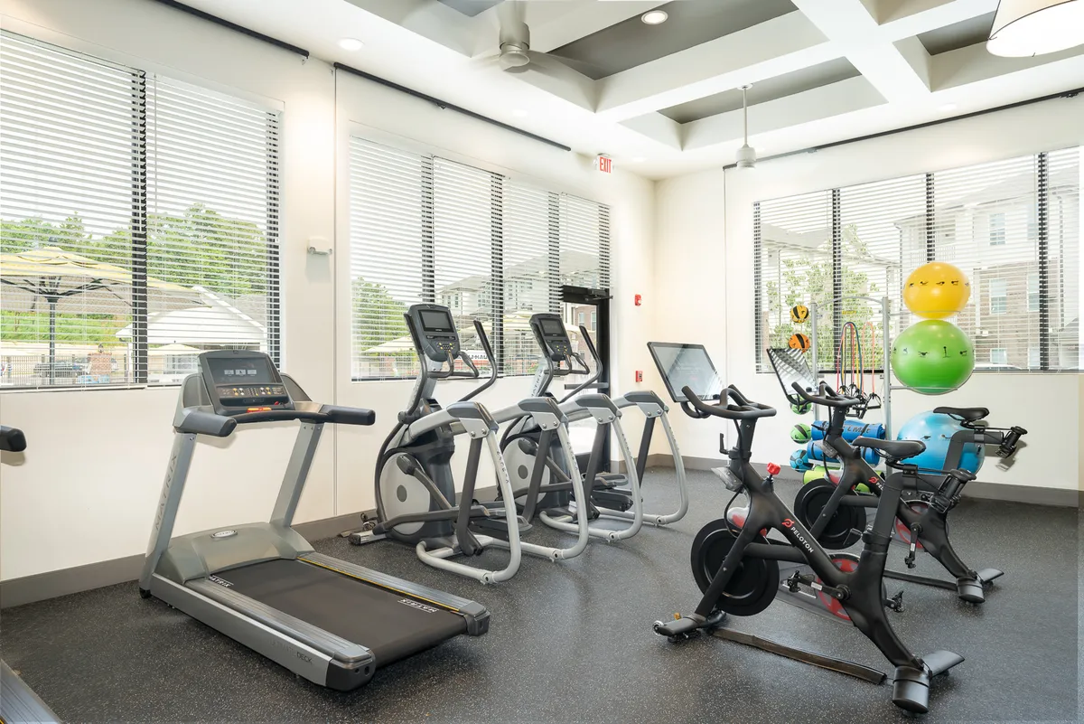 A well-equipped fitness center interior with treadmills, ellipticals, stationary bikes, and exercise balls, set in a spacious and modern environment. The layout invites both individual workouts and community fitness activities.