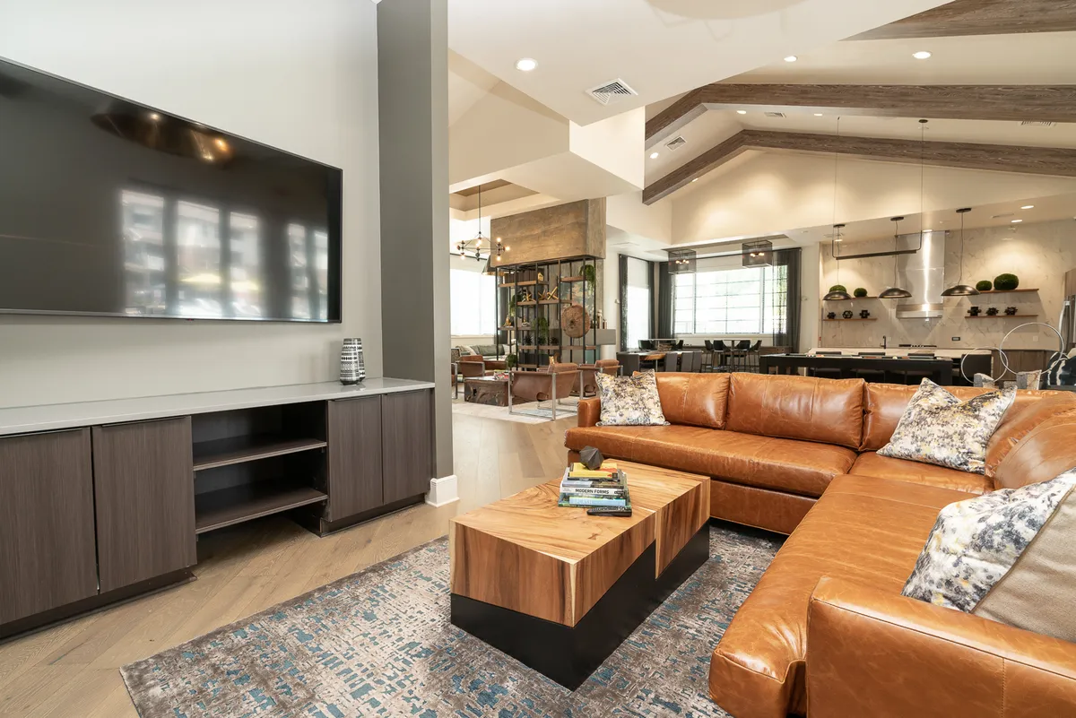 A cozy living space featuring a leather sectional sofa, wood coffee table, and large television, with a dining area visible in the background. The room is stylishly decorated and designed for both relaxation and entertaining guests.