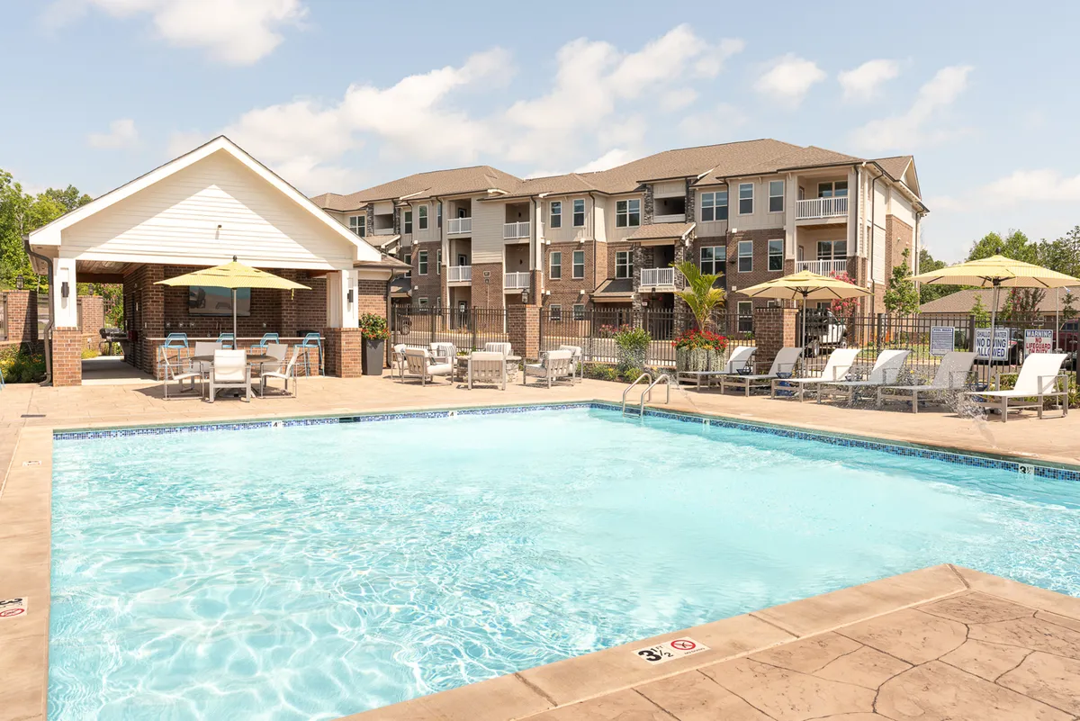 A sparkling swimming pool is surrounded by poolside lounge chairs and a covered pavilion, with the apartment building in the background. The scene is lively and serene, suggesting moments of leisure, social gatherings, and outdoor relaxation after a productive workday.