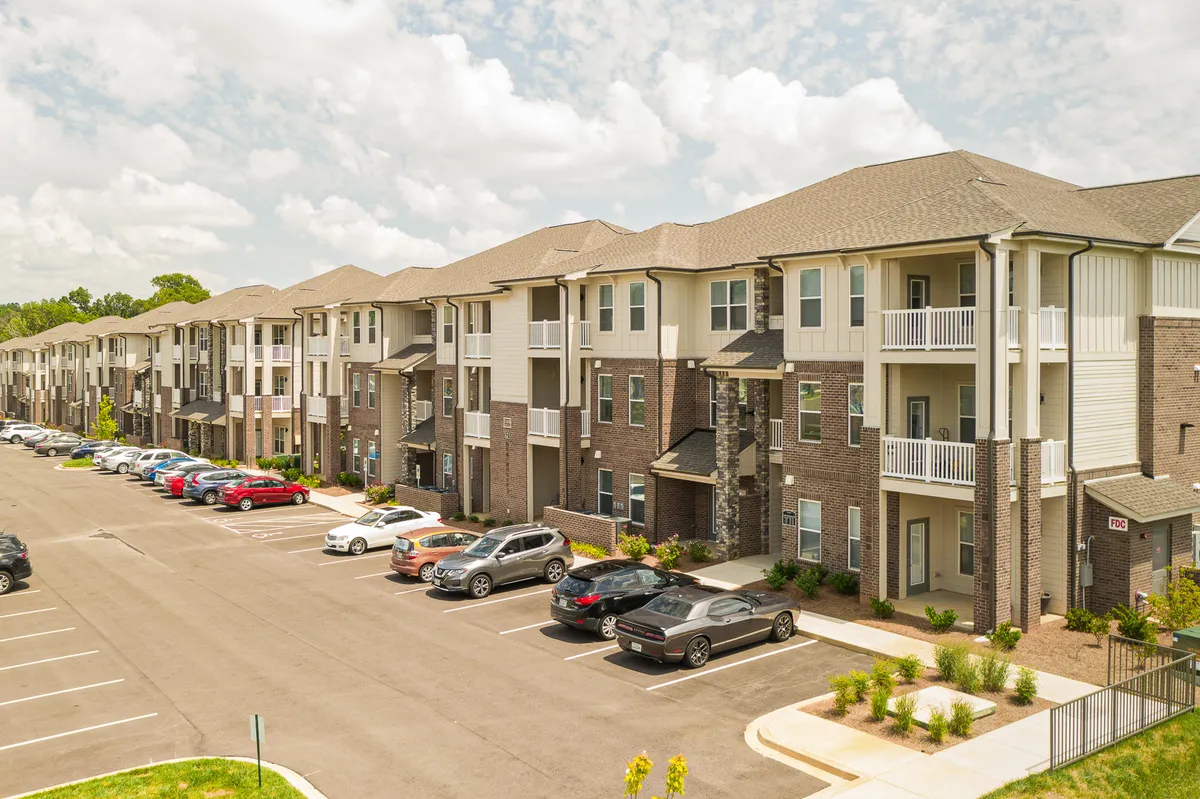 The image captures the exterior of modern apartment buildings with a well-maintained parking lot and landscaped greenery. Clearly marked parking spaces and a welcoming entrance set the tone for resident comfort and security.
