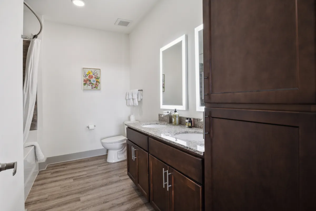 A modern bathroom showcasing a vanity with dual sinks, large mirrors, a walk-in shower, and decorative artwork. The clean lines and quality finishes create a spa-like atmosphere, ideal for self-care and relaxation.